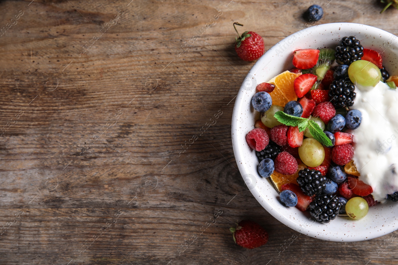 Photo of Fresh tasty fruit salad with yogurt on wooden table, flat lay. Space for text