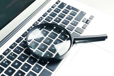 Magnifying glass and modern laptop on table, closeup. Search concept