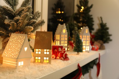 Photo of Christmas atmosphere. Many beautiful glowing houses on window sill indoors