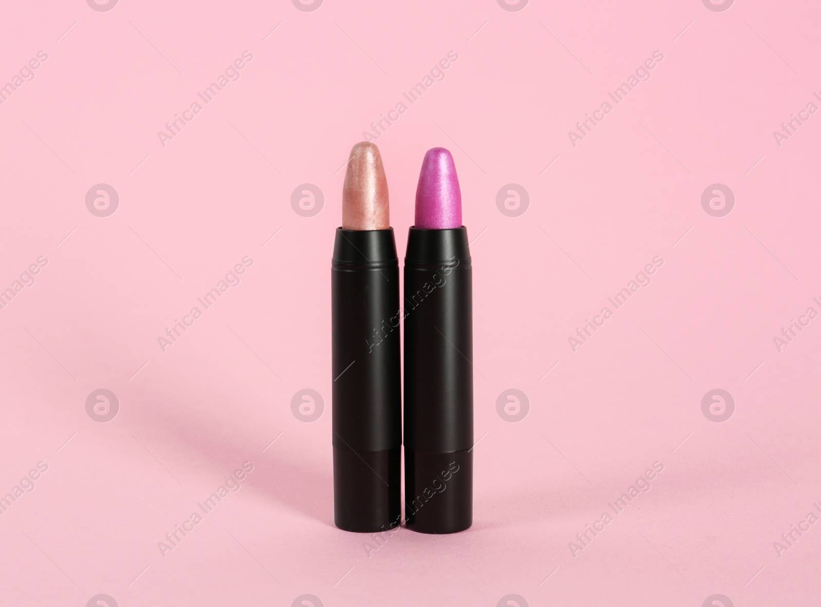 Photo of Bright lipsticks in black tubes on pink background