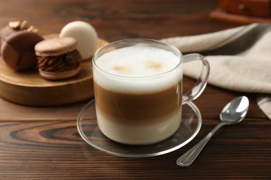 Photo of Aromatic coffee in cup, spoon and macarons on wooden table