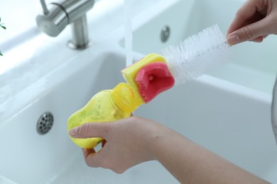 Woman washing baby bottle with brush in kitchen, closeup