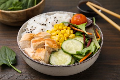 Delicious poke bowl with meat, rice, vegetables and greens on wooden table, closeup