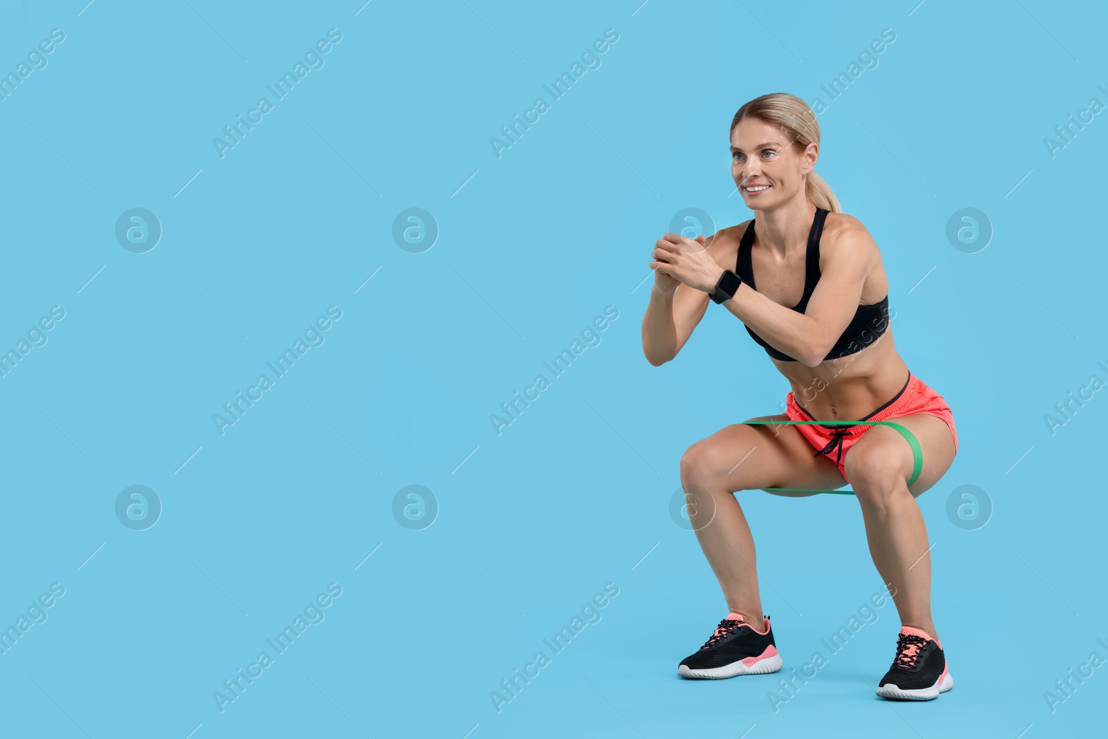 Photo of Woman exercising with elastic resistance band on light blue background. Space for text