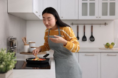 Photo of Beautiful woman cooking and smelling vegetable dish in kitchen. Space for text
