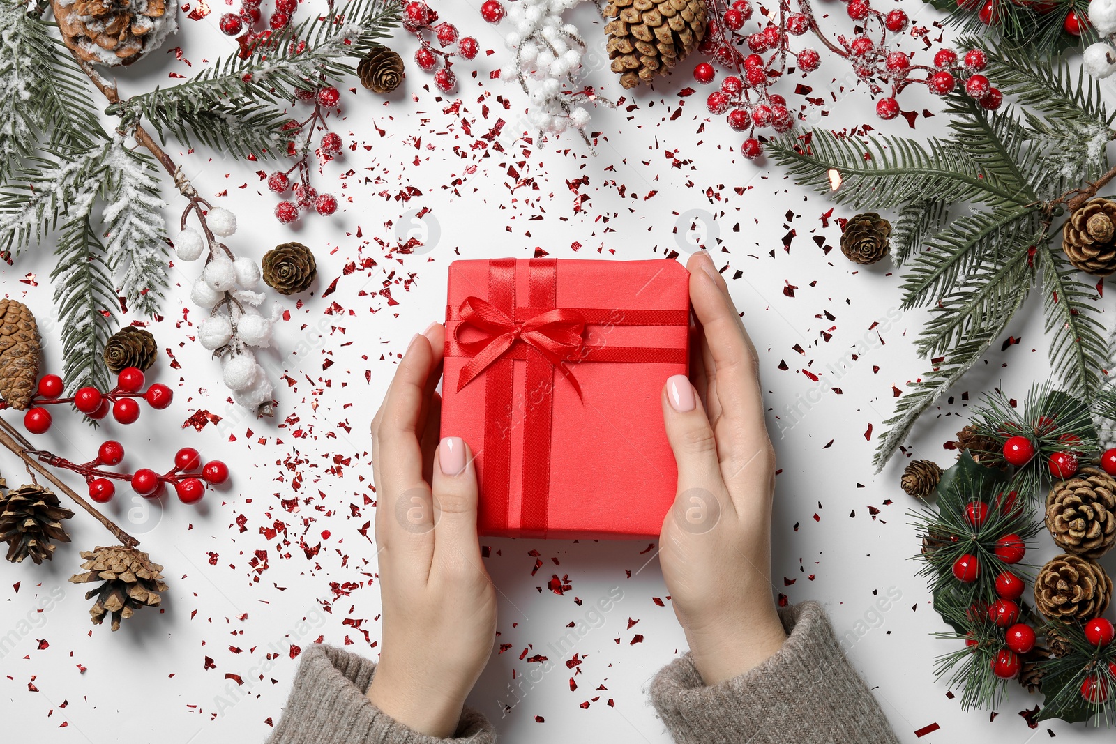 Photo of Christmas present. Woman with gift box, cones, fir tree branches and confetti on white background, top view