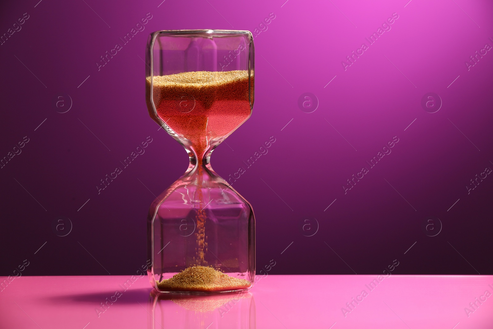 Photo of Hourglass with flowing sand on color background. Space for text