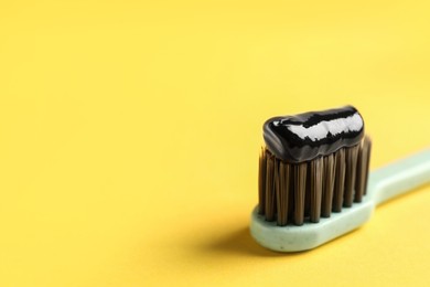 Photo of Brush with charcoal toothpaste on yellow background, closeup. Space for text