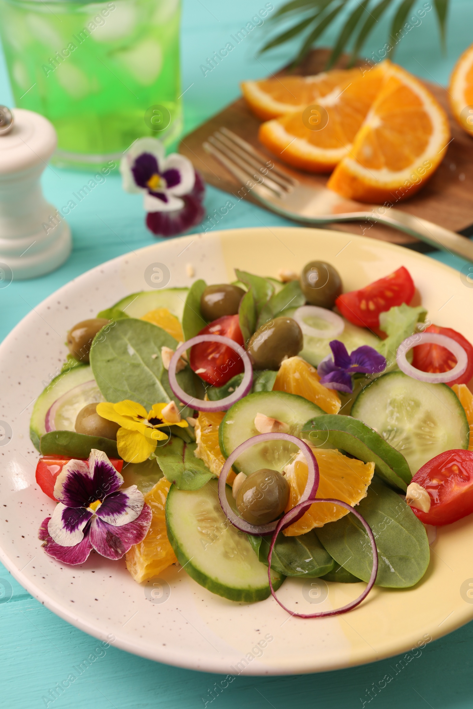 Photo of Delicious salad with orange, spinach, olives and vegetables served on turquoise table, closeup