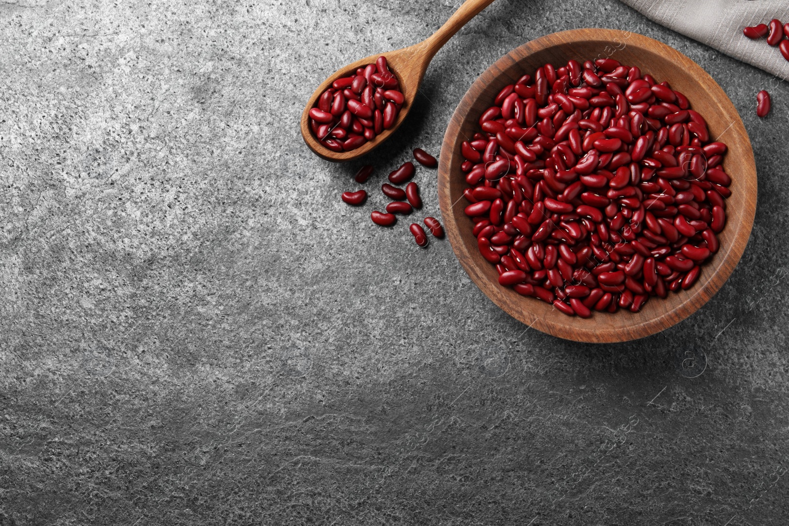 Photo of Raw red kidney beans with wooden bowl and spoon on grey table, flat lay. Space for text