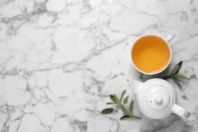 Photo of Cup of sage tea, green leaves and teapot on white marble table, flat lay. Space for text