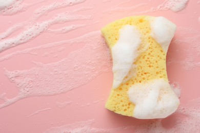 Photo of Yellow sponge with foam on pink background, top view