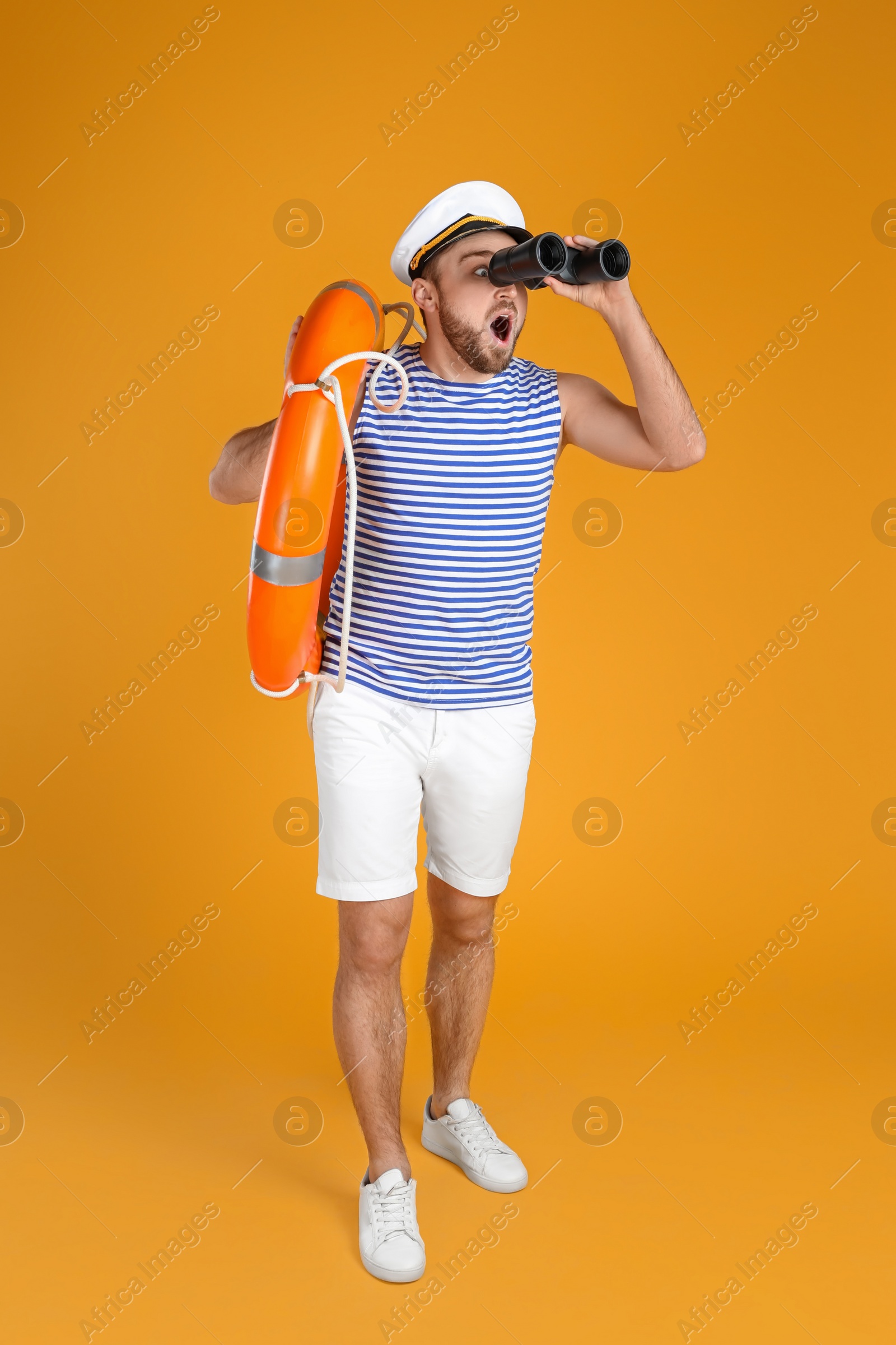 Photo of Emotional sailor with binoculars and ring buoy on yellow background