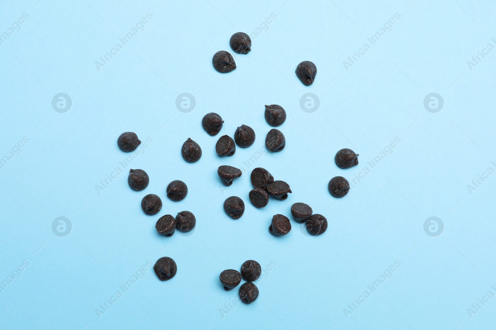 Photo of Delicious dark chocolate chips on light blue background, top view