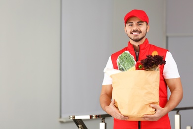 Food delivery courier holding paper bag with products indoors. Space for text