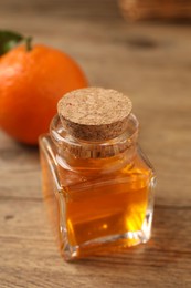 Bottle of tangerine essential oil and fresh fruit on wooden table, closeup