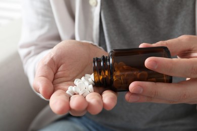 Man pouring pills from bottle on blurred background, closeup