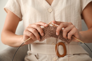 Young woman knitting with needles indoors, closeup. Engaging in hobby