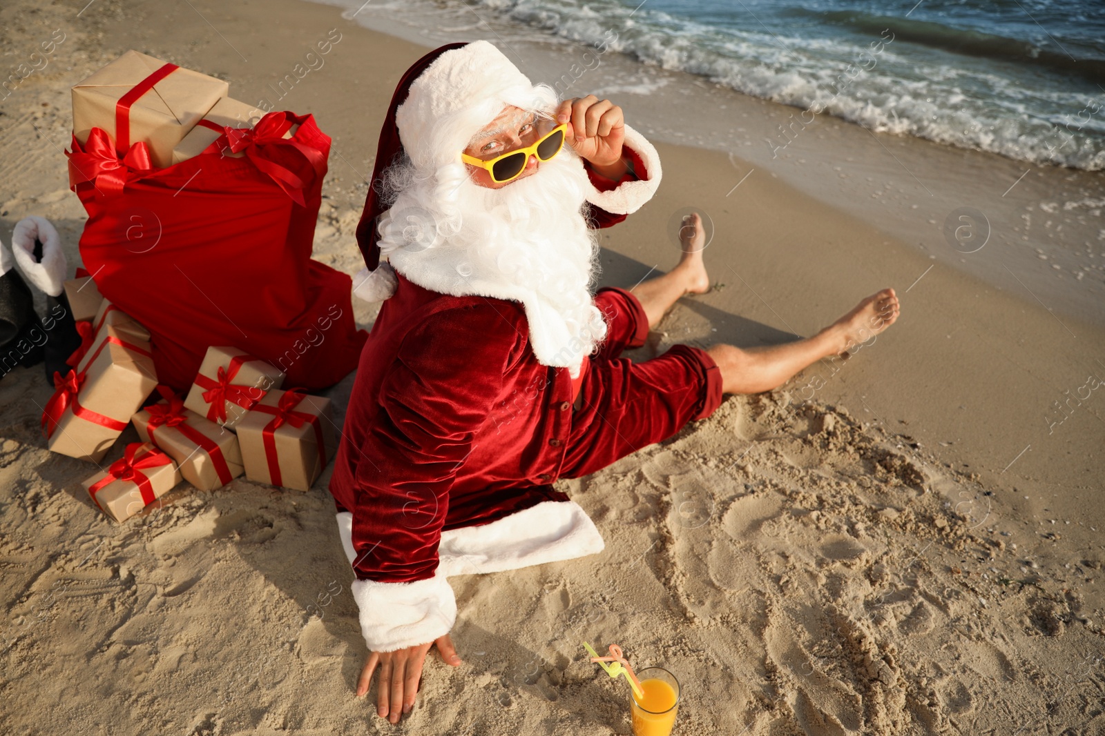 Photo of Santa Claus with cocktail and bag of presents relaxing on beach. Christmas vacation