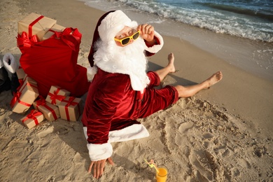 Santa Claus with cocktail and bag of presents relaxing on beach. Christmas vacation