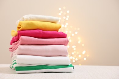 Photo of Stack of folded clothes on wooden table against beige background with blurred lights, space for text