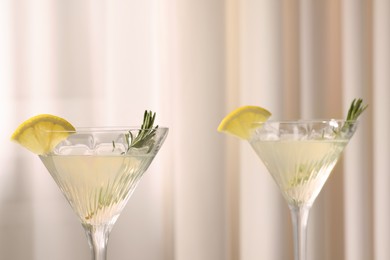 Elegant martini glasses with fresh cocktail, rosemary and lemon slices near curtain