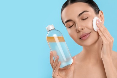 Beautiful woman removing makeup with cotton pad on light blue background, space for text