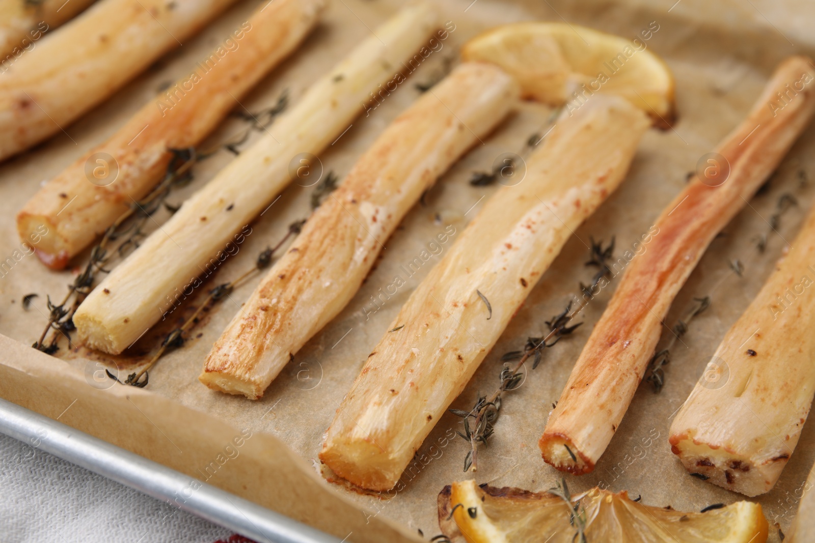 Photo of Baking tray with cooked salsify roots, lemon and thyme on table, closeup