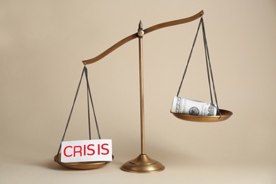 Photo of Scale with word Crisis and money on beige background
