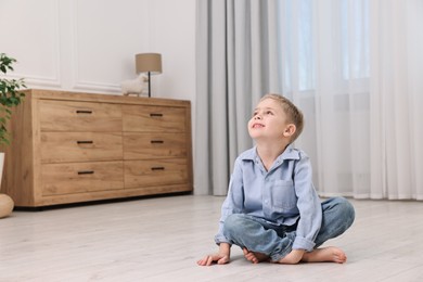 Cute little boy sitting on warm floor at home, space for text. Heating system