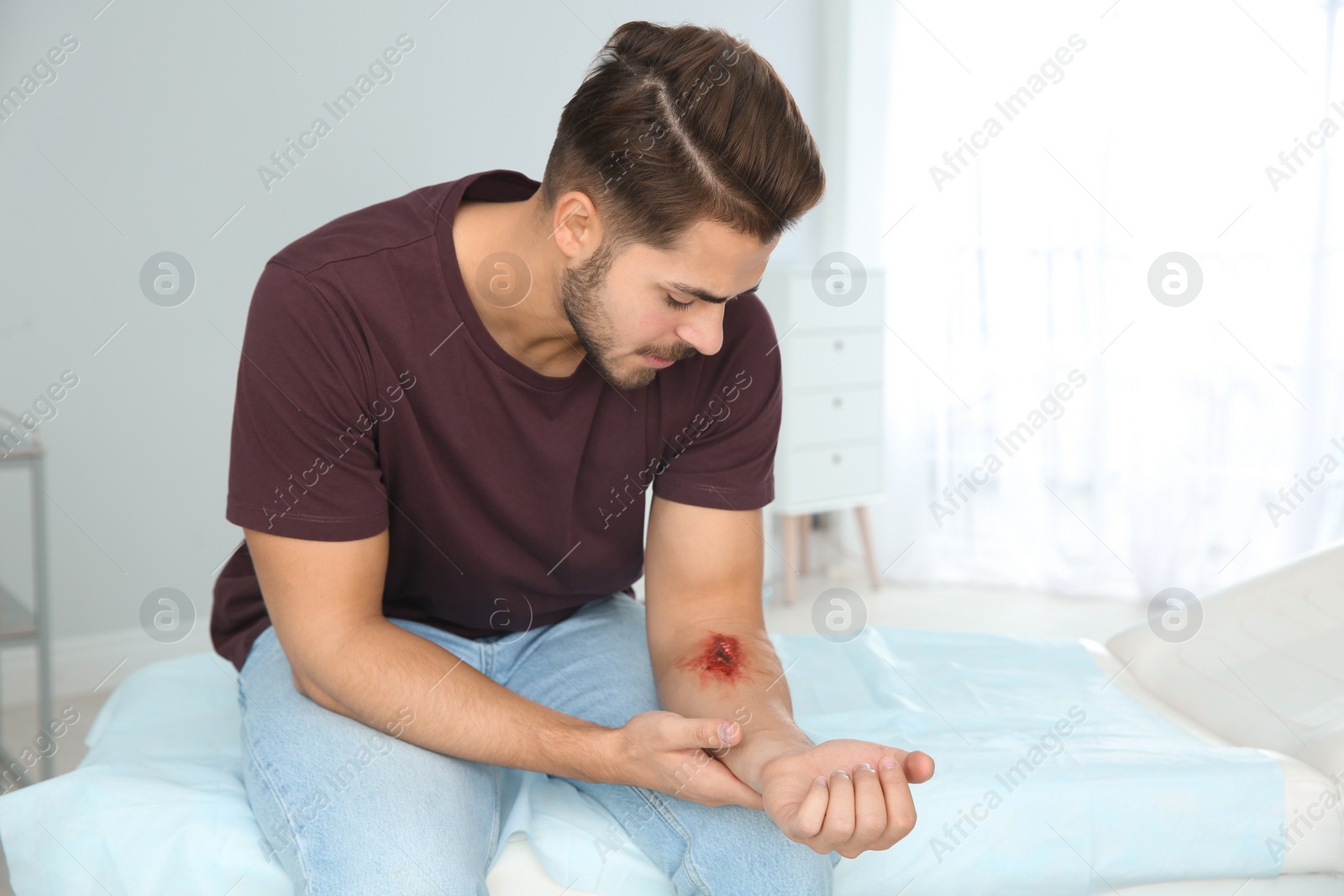 Photo of Young man with injured arm in clinic. First aid