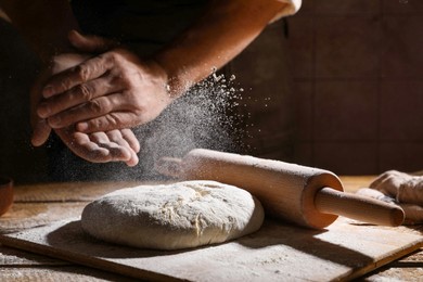 Photo of Man sprinkling flour over dough at wooden table, closeup