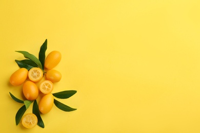 Photo of Fresh ripe kumquats with green leaves on yellow background, flat lay. Space for text