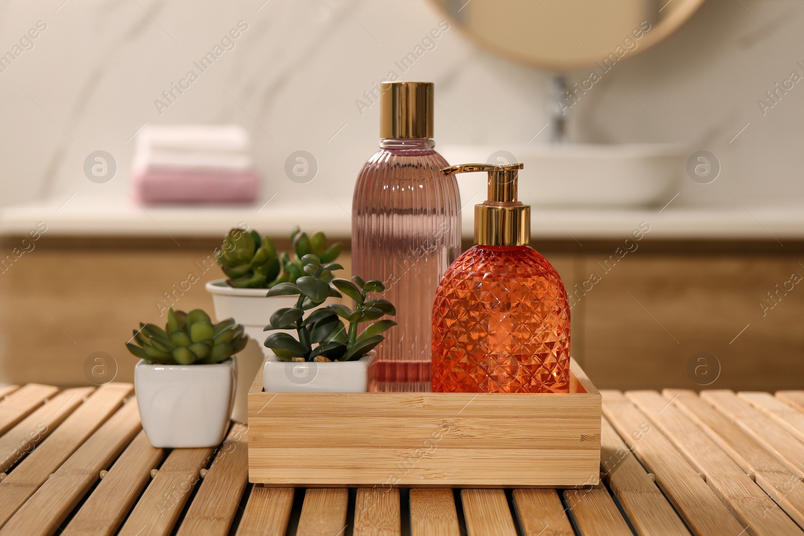 Photo of Glass dispenser with liquid soap, bottle of gel and plants on wooden table in bathroom