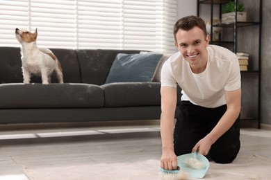 Photo of Smiling man with brush and pan removing pet hair from carpet at home. Space for text