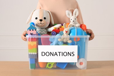 Photo of Little girl holding donation box with toys against light background, closeup