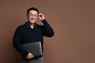 Portrait of happy man with laptop on brown background. Space for text