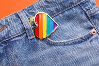 Photo of Jeans with rainbow heart shaped pendant on orange background, top view. LGBT pride