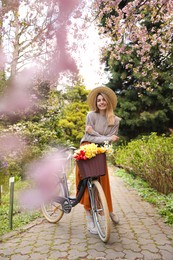 Photo of Beautiful young woman with bicycle and flowers in park on pleasant spring day