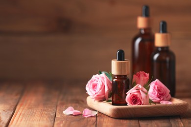 Photo of Bottles of essential rose oil and flowers on wooden table, space for text