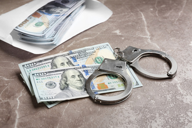 Photo of Dollar bills and handcuffs on brown marble table. Bribe concept