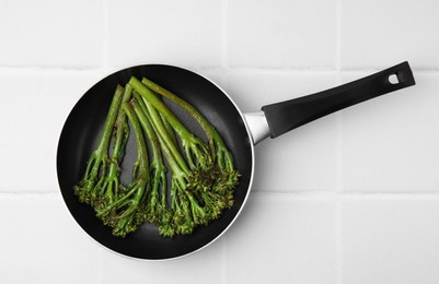 Photo of Frying pan with tasty cooked broccolini on white tiled table, top view
