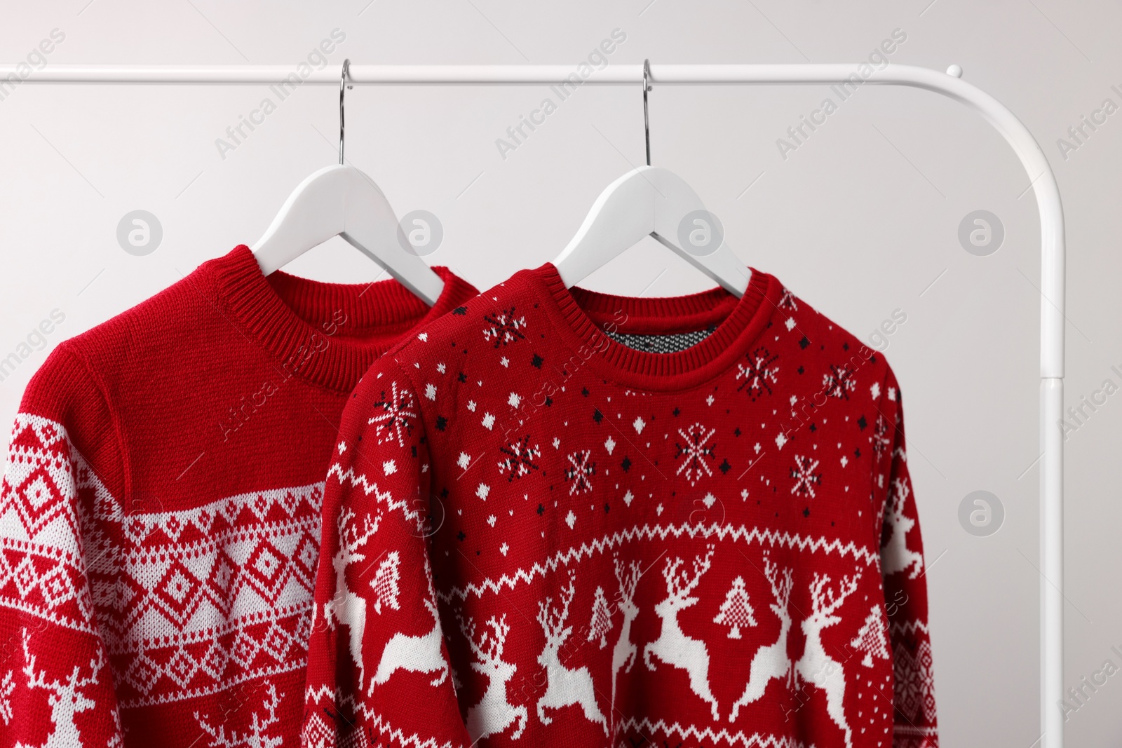 Photo of Rack with Christmas sweaters on light background