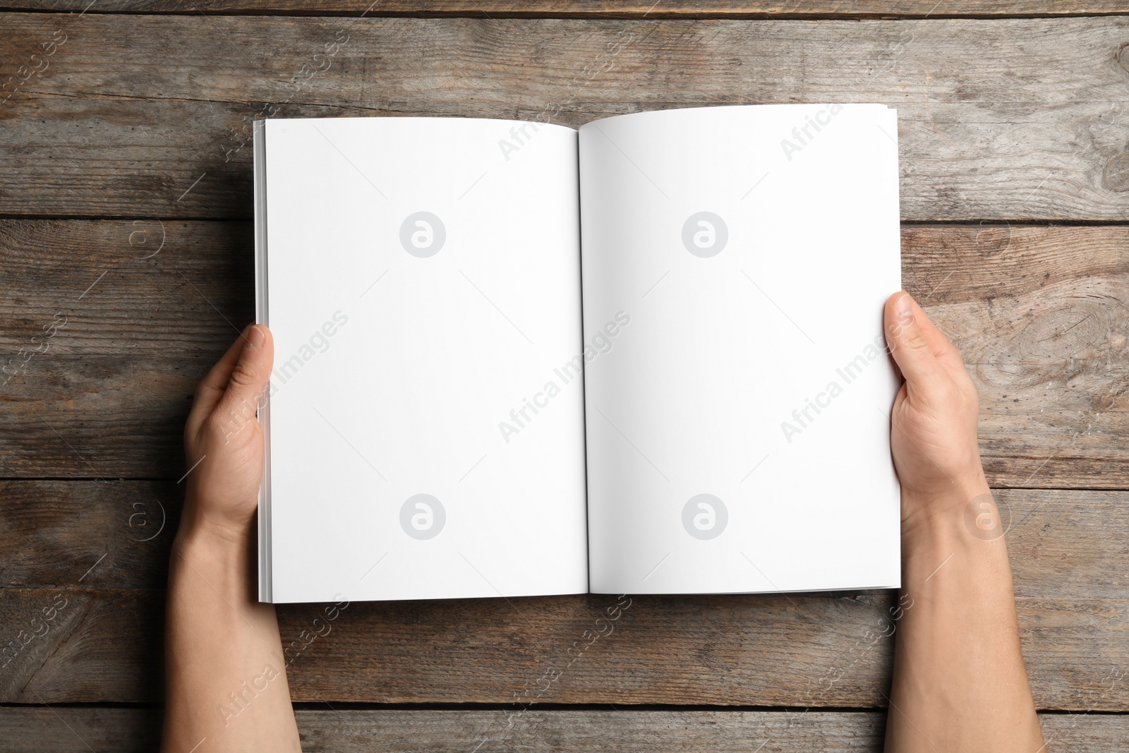 Photo of Woman holding brochure with blank pages on wooden background, top view. Mock up for design