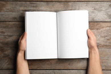 Photo of Woman holding brochure with blank pages on wooden background, top view. Mock up for design