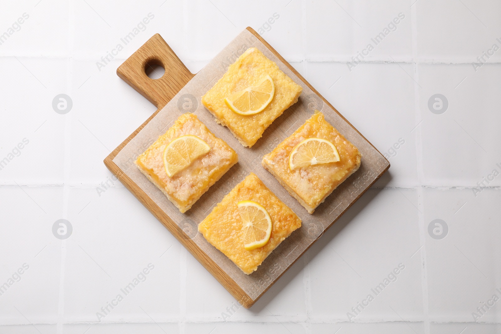 Photo of Tasty lemon bars on white tiled table, top view