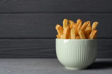 Photo of Bowl of french fries on grey wooden table, space for text