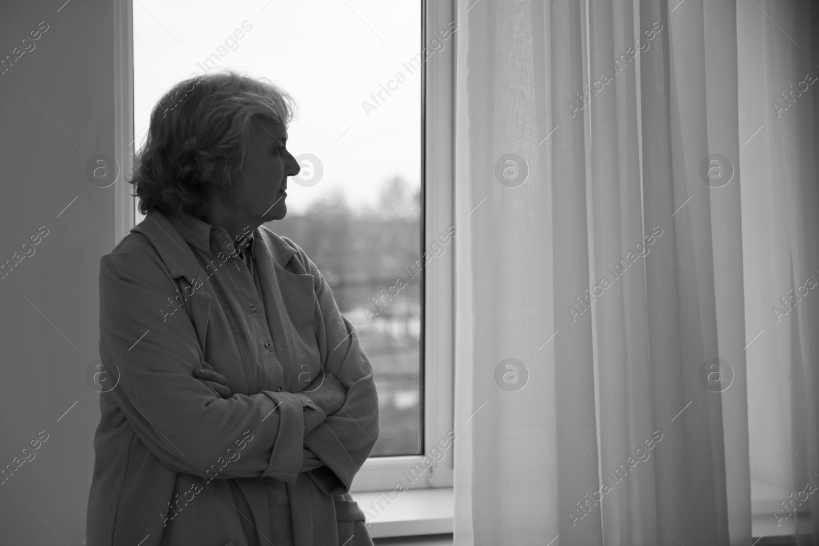 Photo of Portrait of elderly woman near window indoors, space for text. Black and white effect