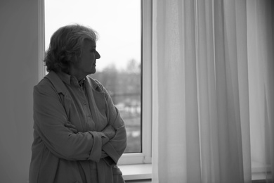 Photo of Portrait of elderly woman near window indoors, space for text. Black and white effect