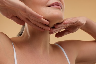 Photo of Mature woman touching her neck on beige background, closeup